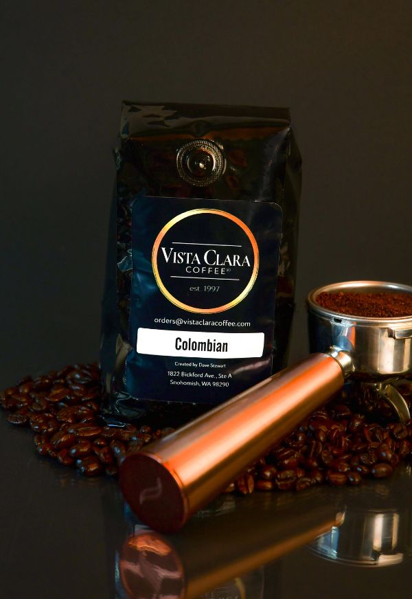 Vista Clara Coffee bag labeled Colombian with a portafilter and coffee beans on a reflective surface