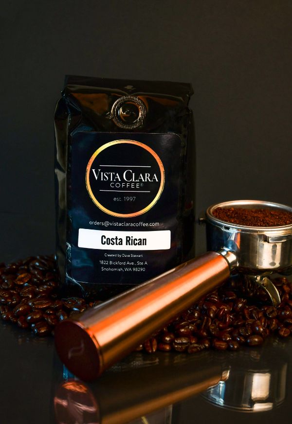 Vista Clara Coffee bag labeled Costa Rican with a portafilter and coffee beans on a reflective surface.