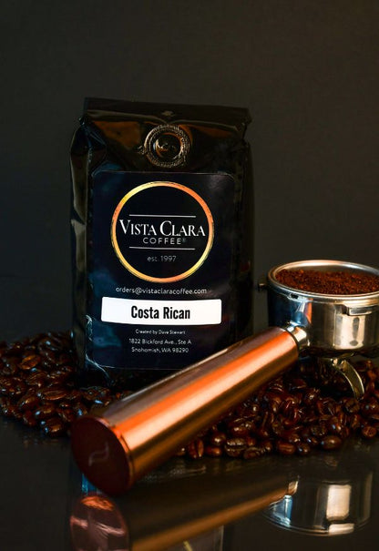 Vista Clara Coffee bag labeled Costa Rican with a portafilter and coffee beans on a reflective surface.