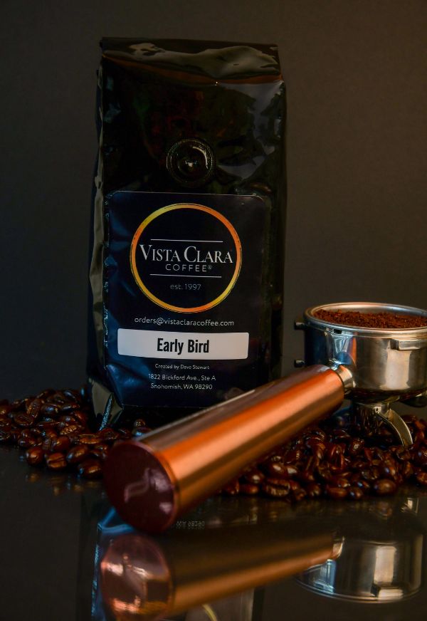 Vista Clara Early Bird coffee bag with portafilter and scattered beans on a dark surface.