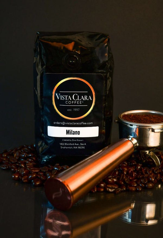 Vista Clara Milano coffee bag with portafilter and scattered beans on a dark surface.