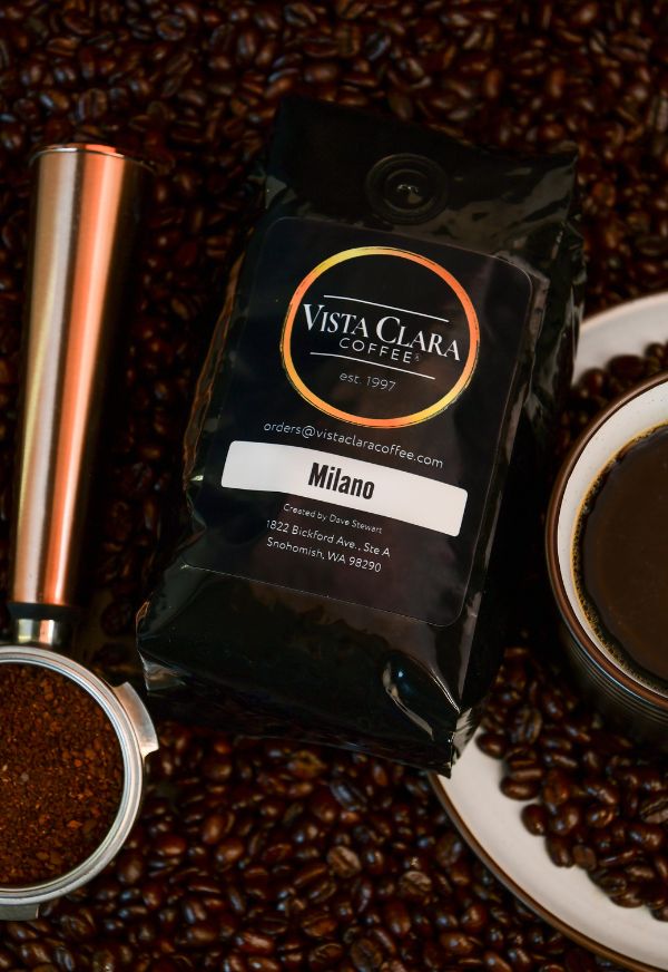 Bag of Vista Clara  Milano coffee surrounded by beans, with a copper grinder and fresh coffee in a cup