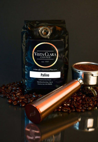 Vista Clara Pallino coffee bag with portafilter and scattered beans on a dark surface.