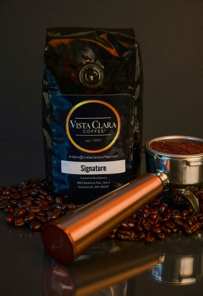 Vista Clara Signature coffee bag with portafilter and scattered beans on a dark surface.