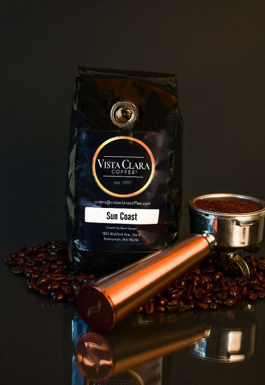 Vista Clara Sun Coast coffee bag with portafilter and scattered beans on a dark surface.